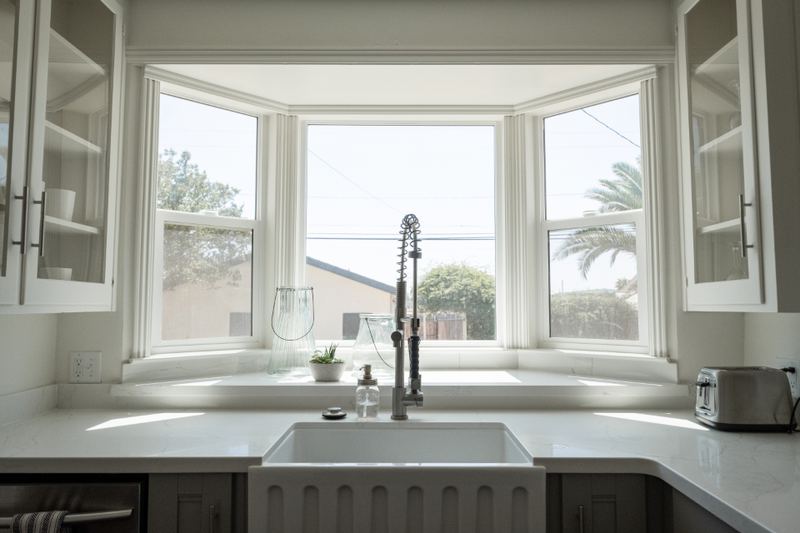 Clean kitchen sink and countertop beside a bright bay window