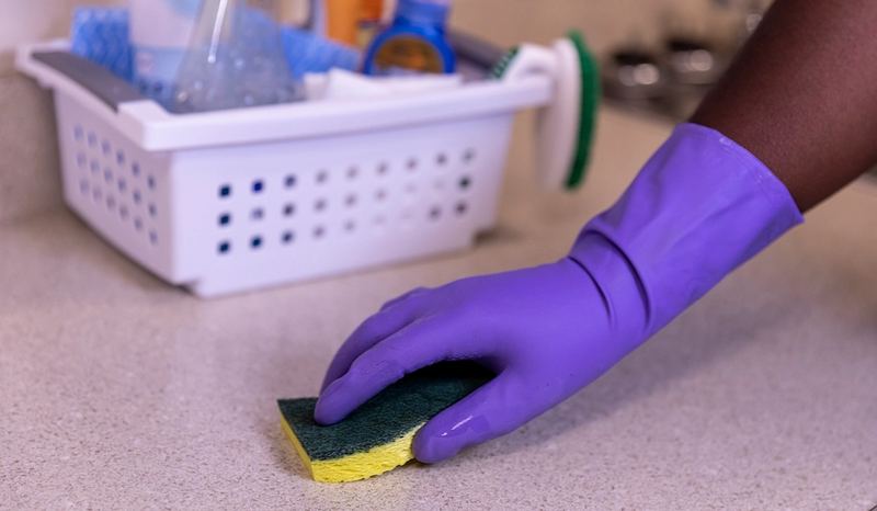 Gloved hand disinfecting a hard surface with a sponge